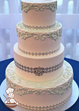 4-tier cake with smooth white icing and buttercream mint-green scrolls and a rhinestone band on each tier.