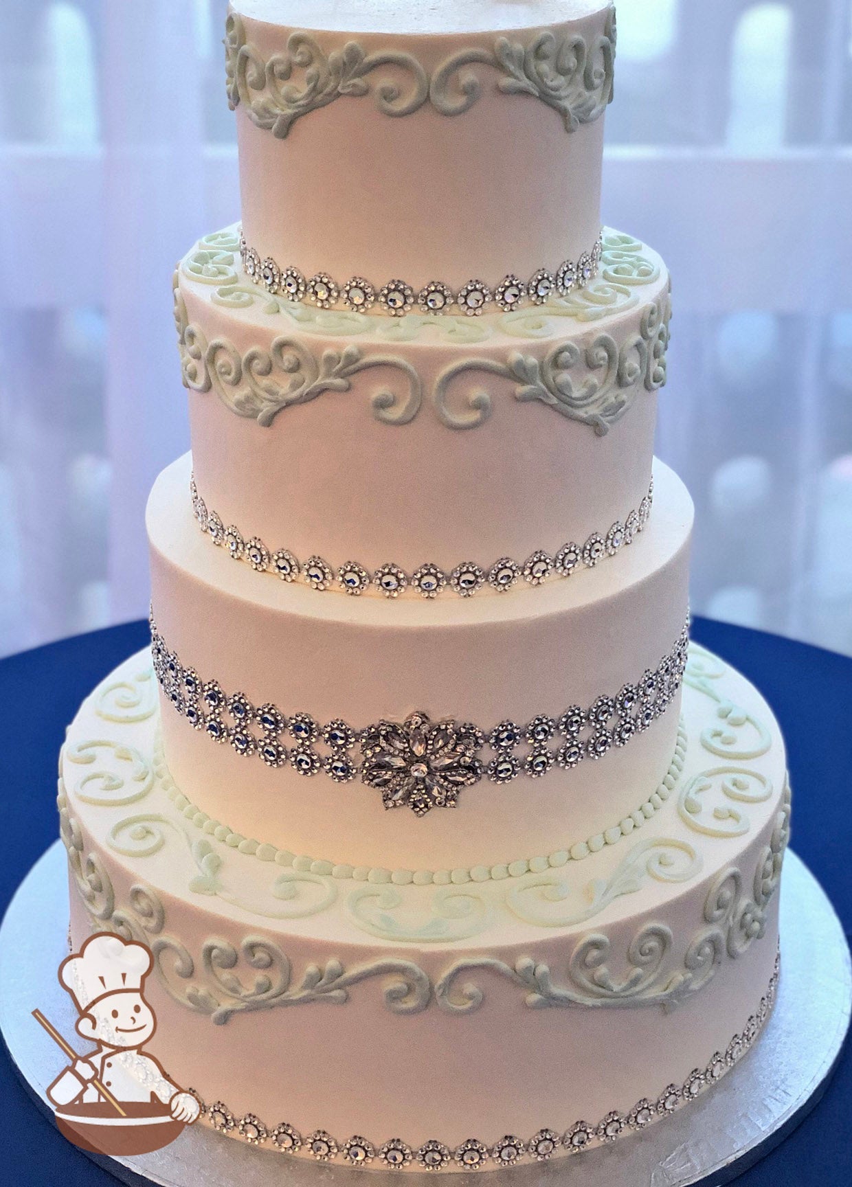 4-tier cake with smooth white icing and buttercream mint-green scrolls and a rhinestone band on each tier.