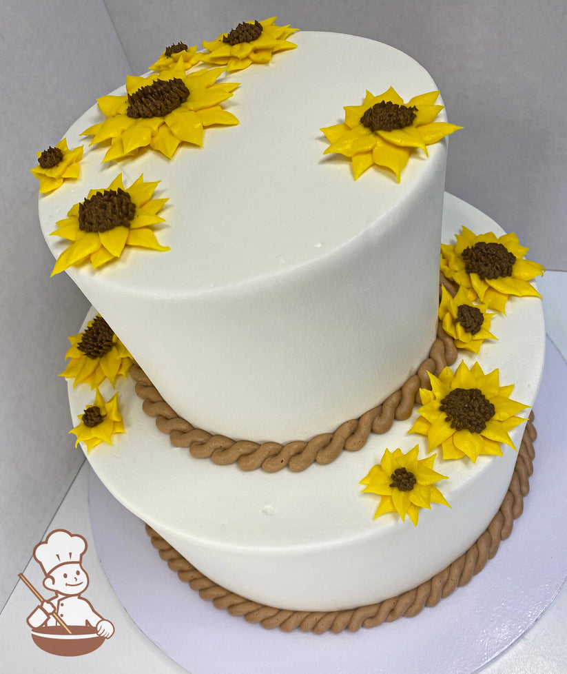 Two-tier round cake with buttercream sunflowers scattered on tiers and rope trims on both bottoms of tiers.