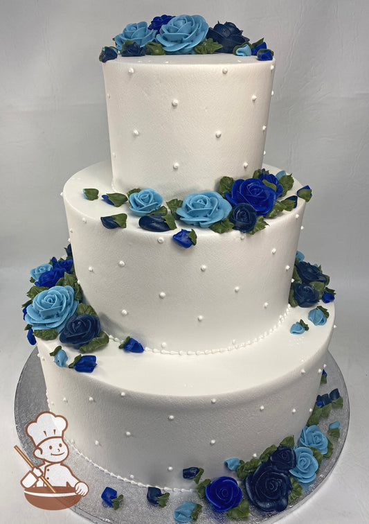Three-tier round cake with buttercream roses and rosebuds in different shades of blue, white buttercream dots on cake walls and white bead trims.