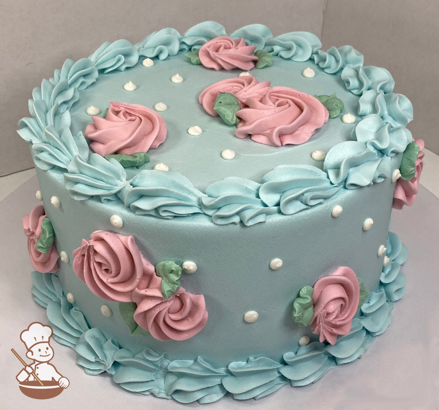 Single-tier round cake with smooth light blue icing and large shell trims on top and bottom of cake with light pink swirlettes and white dots.