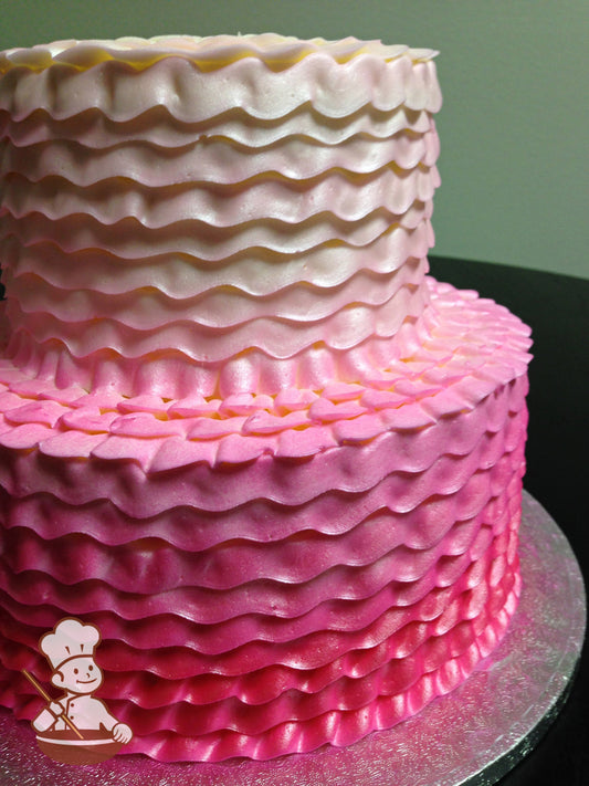 2-tier round cake with a buttercream ruffle texture and Ombre-colored icing starting from hot pink at the bottom of the cake to white on the top.