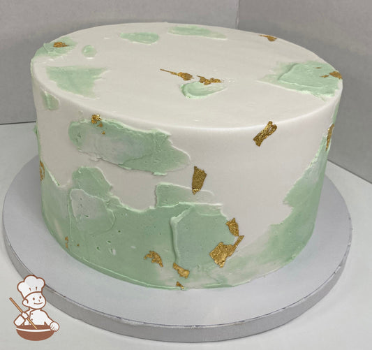 Single tier round cake with white icing and added texture in a pastel green color with gold foil flakes all over cake.