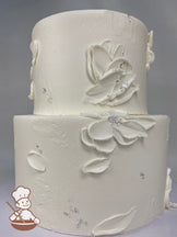 2-tier round cake with white icing and palette knife flowers and a some silver foil flakes on the cake walls.