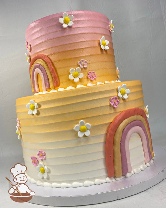 2-tier round cake with horizontal texture icing and pink and orange icing. The cake also has buttercream rainbows and sugar daisies.