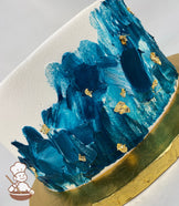 Single tier cake with smooth white icing, decorated with ocean-blue painted texture and gold foil flakes.