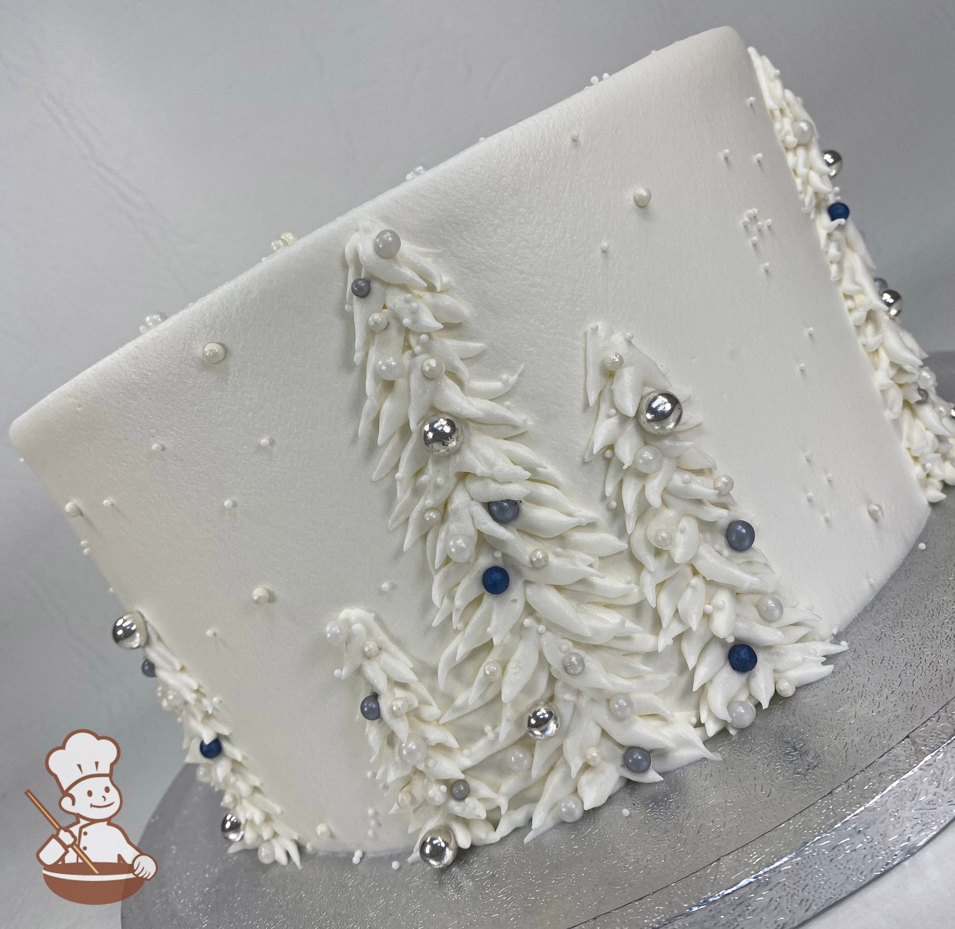 Single tier cake with smooth white icing and buttercream white trees with silver, white, gray and blue sugar pearls.