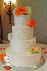 4-tier cake with smooth white icing and decorated with white buttercream scrolls and fresh flowers.