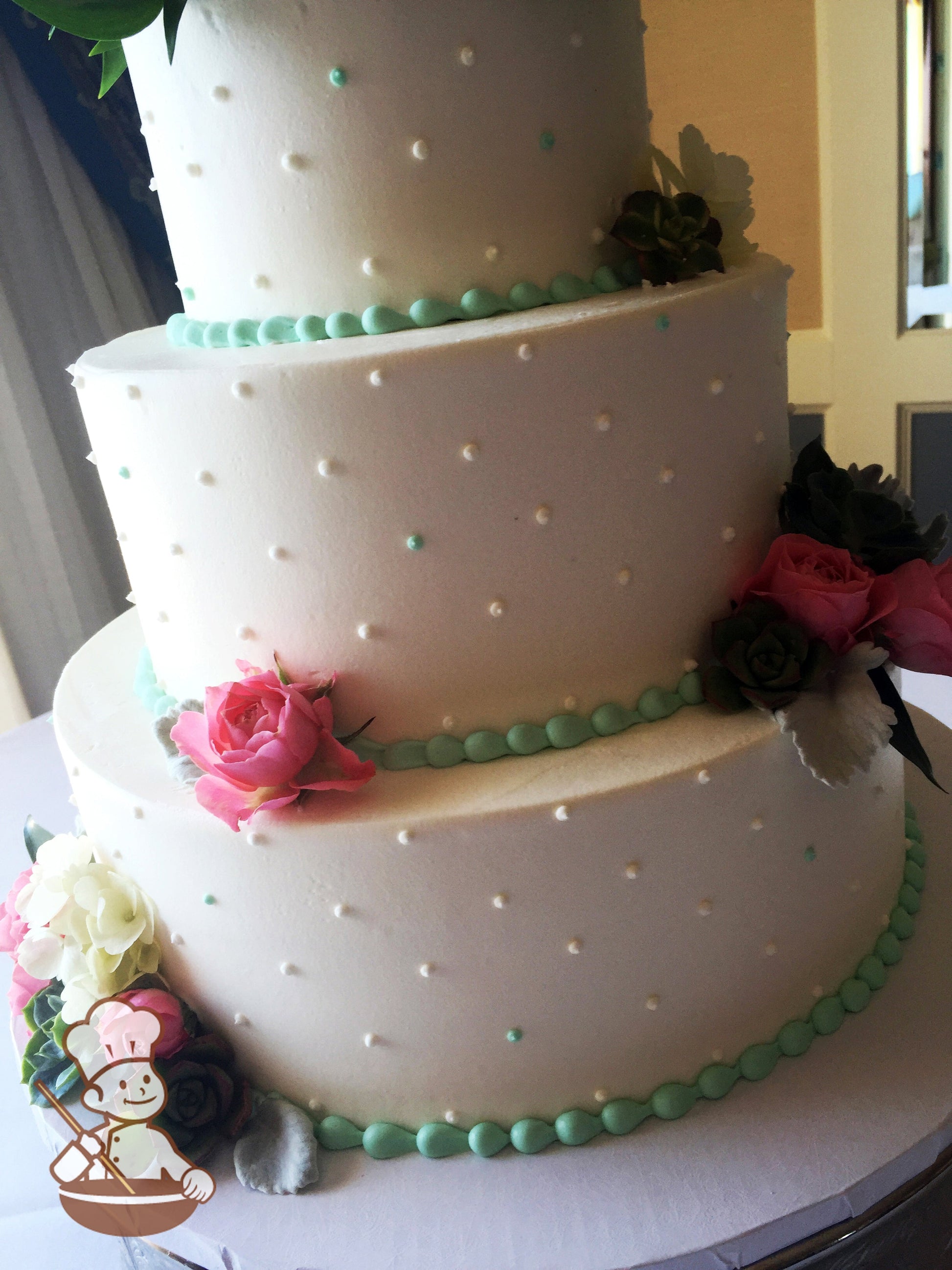 3-tier white cake with smooth white icing and decorated with white and aqua-color buttercream dots and aqua-color beaded trims and fresh flowers.