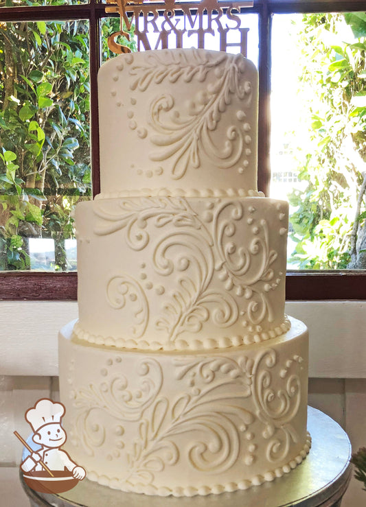 3-tier cake with smooth white icing and decorated with white buttercream scrolls and white buttercream beaded trims.