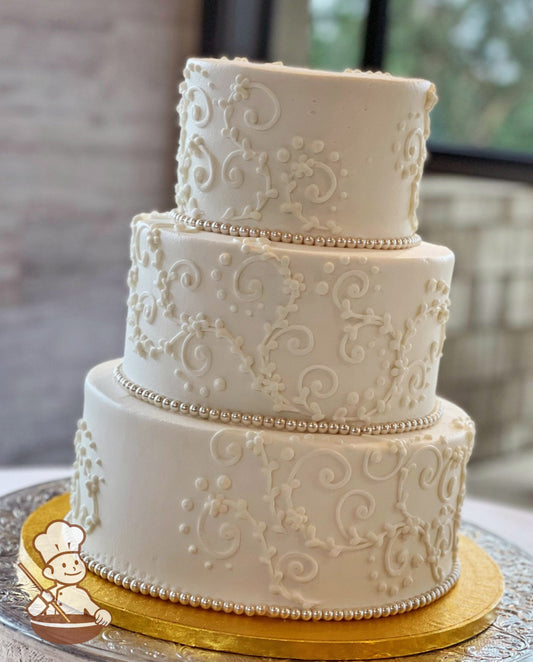 3-tier cake with smooth white icing and decorated with white buttercream scrolls and glass beaded trims.