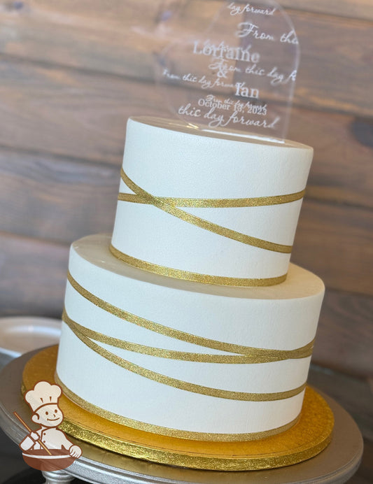 2-tier cake with smooth white icing and gold shimmery ribbon placed criss-cross all over the cake.