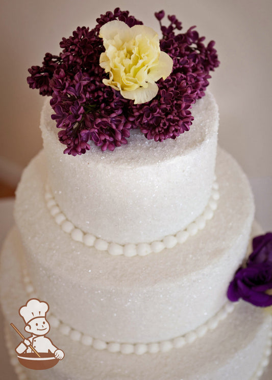Round buttecream 3 tier wedding cake covered with sugar crystal and finished with fresh flowers.