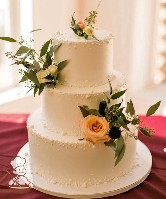 Buttercream icing 3 tier round wedding cake with buttercream pearl bead decoration and fresh flowers.