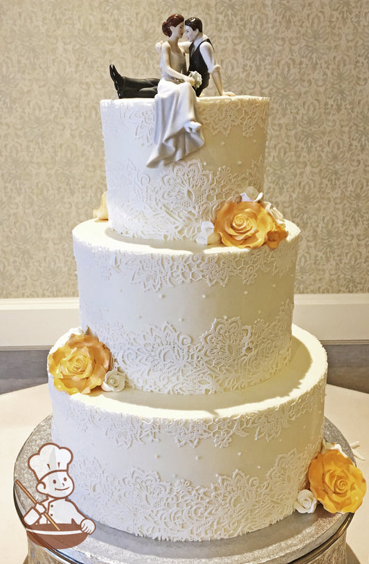 3 tier round buttercream icing wedding cake decorated with white sugar lace on all 3 tiers and finished with gold and white sugar roses.