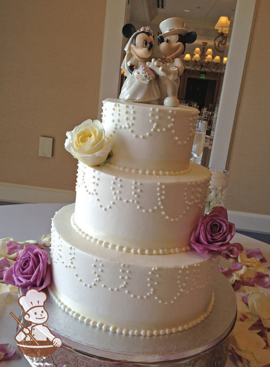 3 Tier Buttercream wedding cake with bead strand piping and fresh floral decoration.  Cake is topped with Mickey & Minnie figurine.