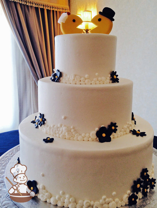 3 Tier round wedding cake with buttercream beaded piping on base of each tier and decorated with navy blue daisies.  Pac Man cake topper.