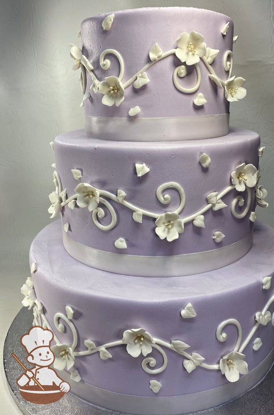 3 tier round periwinkle colored buttercream cake with white piping and decorated with white sugar flowers.