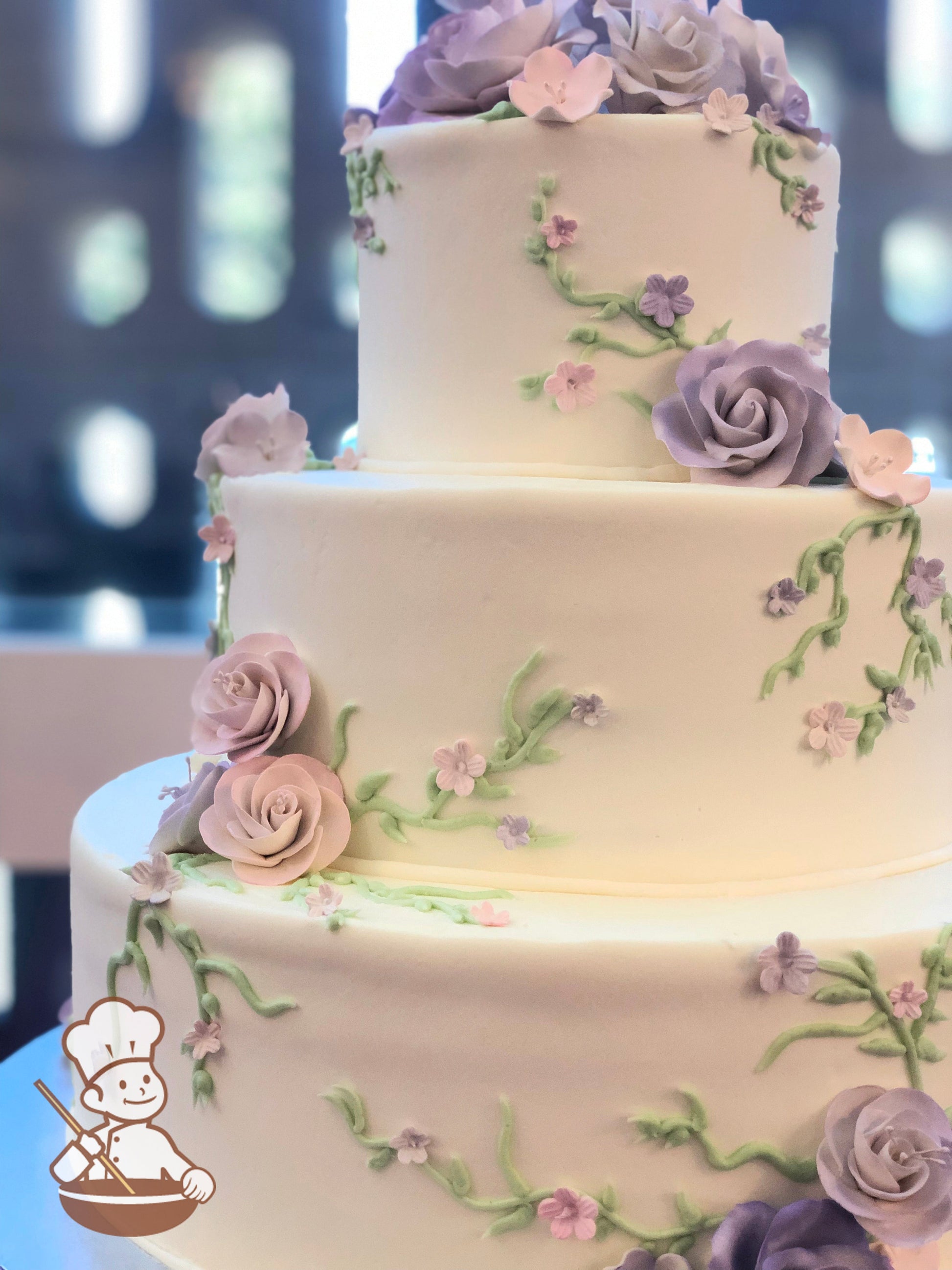 3 tier round wedding cake in buttercream with vine piping and fondant and sugar flowers decorations in pinks and purples.