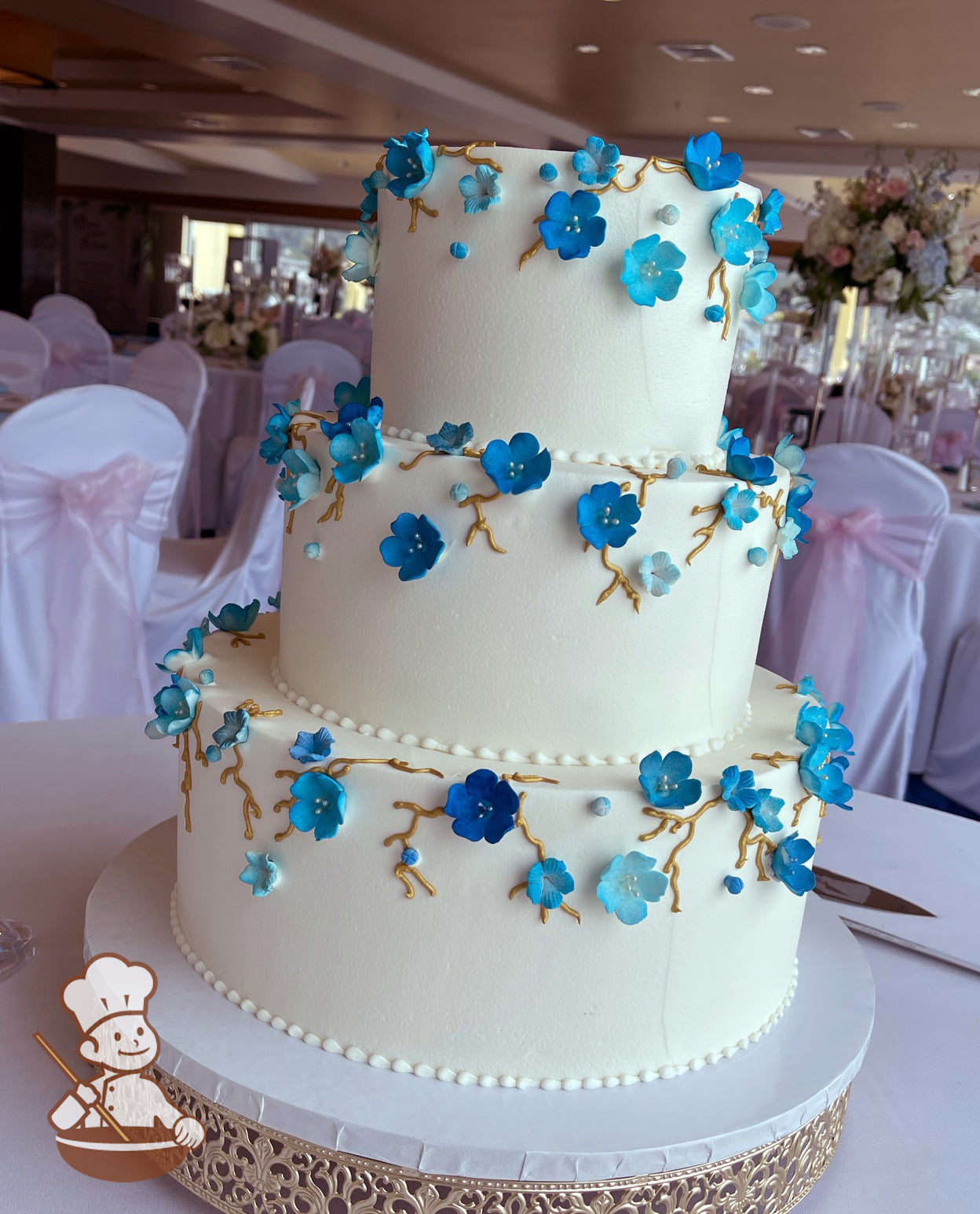 3 tier buttercream wedding cake with gold vine piping and sugar hydrangeas in blue tones.