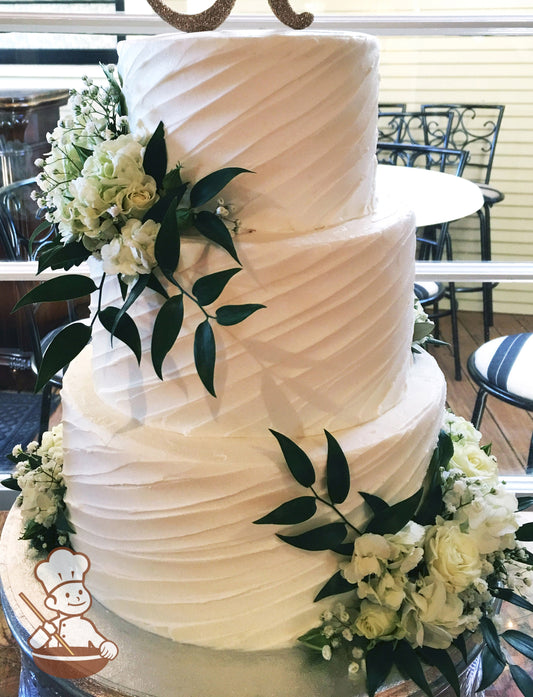 3-tier cake with white icing and decorated with a diagonal angle texture and white fresh flowers.