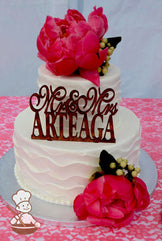 2-tier cake with white icing and decorated with a wavy texture and white beaded trims.