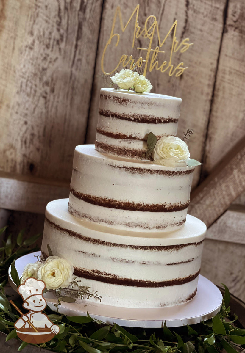 3-tier cake with white icing and decorated with a scraped texture to show some of the cake and white fresh flowers.