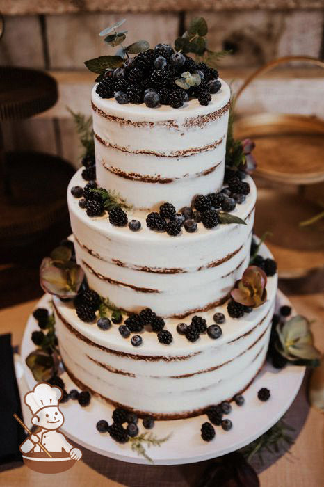 3-tier cake with white icing and decorated with a scraped texture to show some of the cake and fresh blackberries and blueberries.