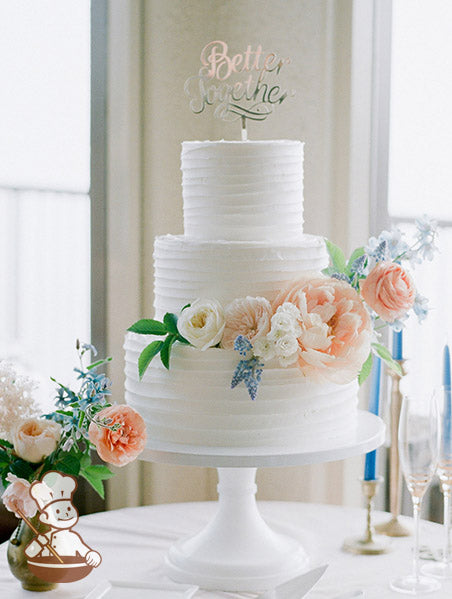 3-tier cake with white icing and decorated with a horizontal texture and fresh flowers.