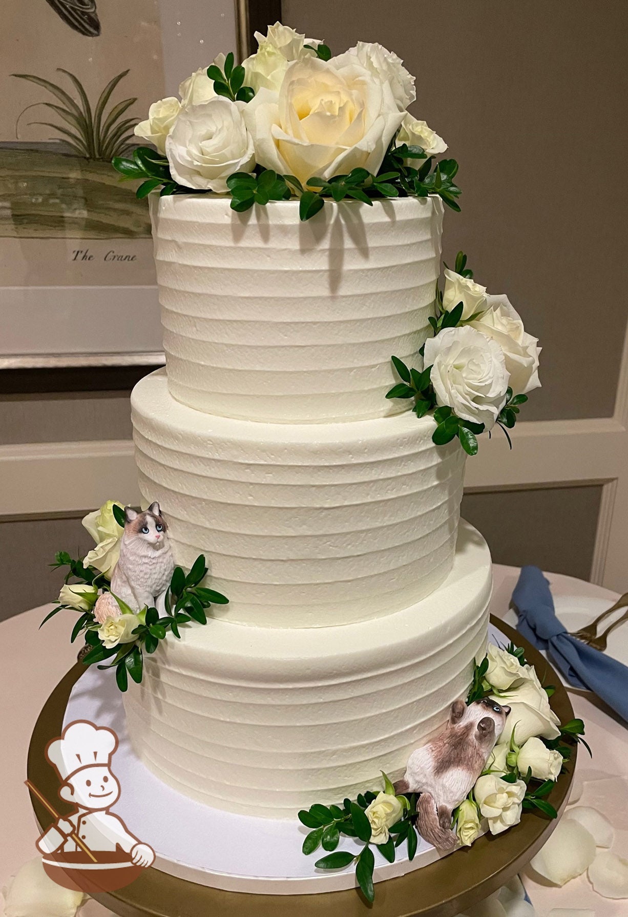 3-tier cake with white icing and decorated with a horizontal texture and fresh flowers in white and cream colors.