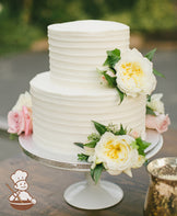 2-tier cake with white icing and decorated with a horizontal texture and fresh flowers.