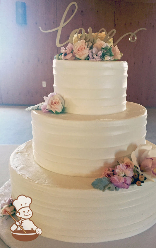 3-tier cake with white icing and decorated with a light horizontal texture and fresh flowers.
