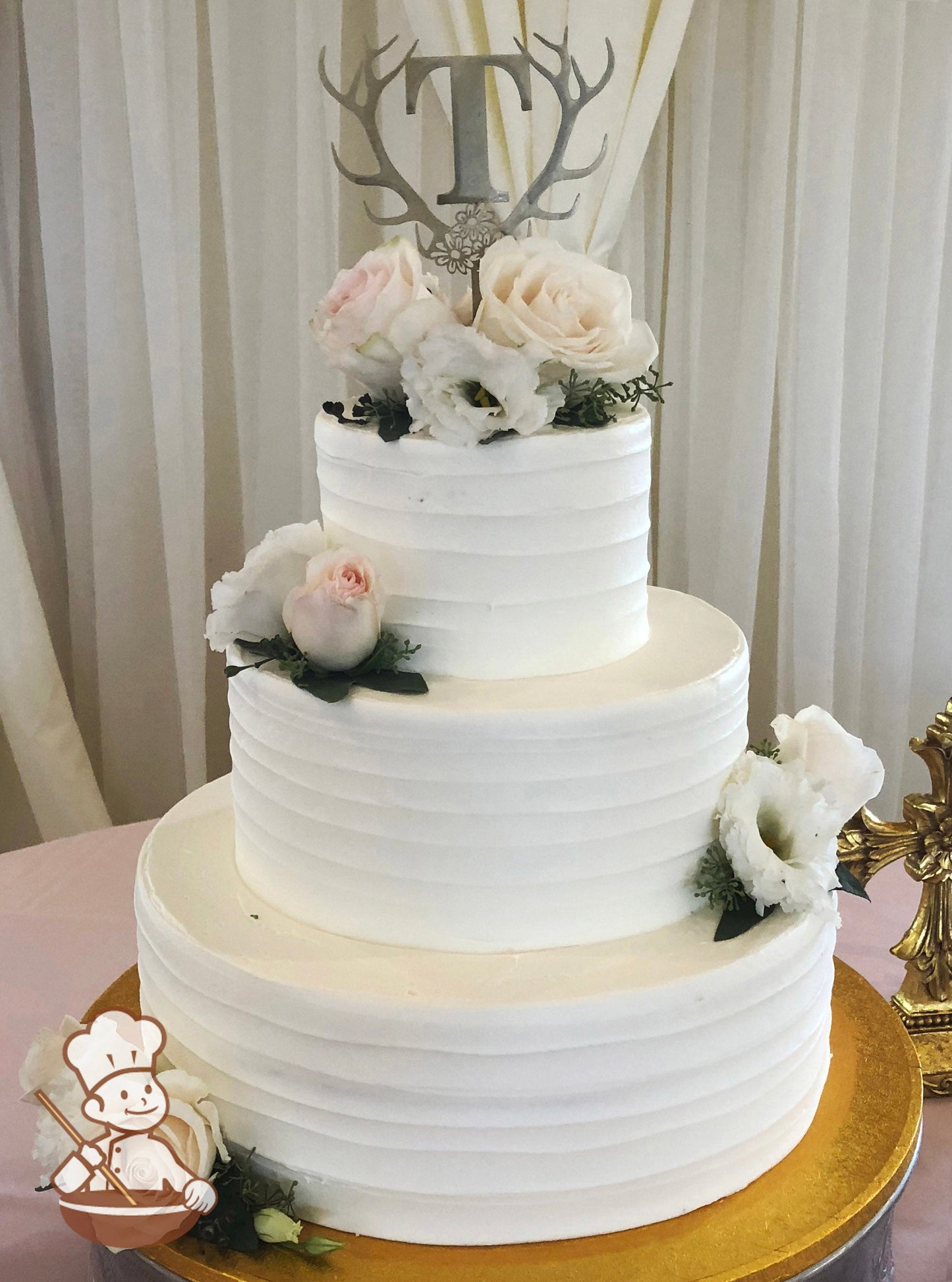 3-tier cake with white icing and decorated with a light horizontal texture and fresh flowers in pink and white colors.