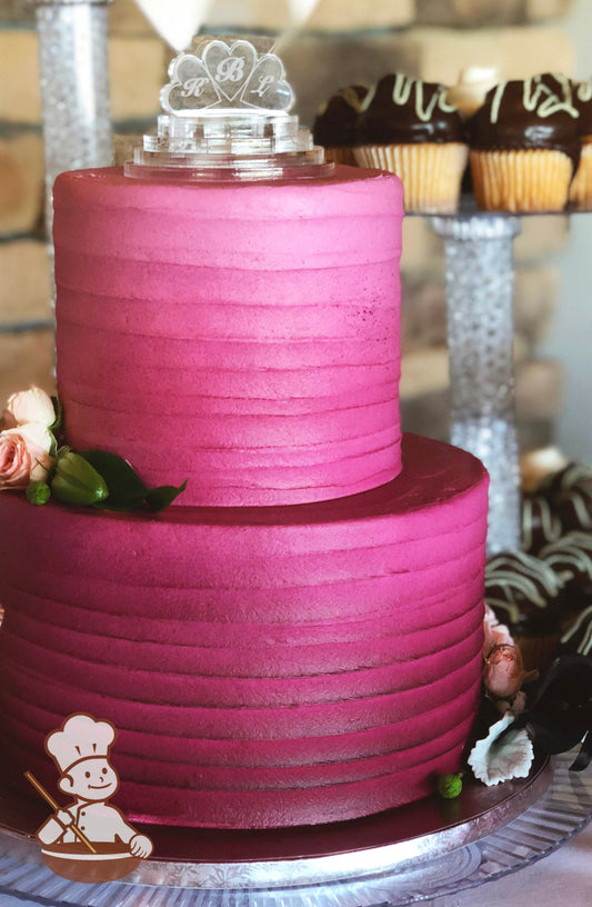 2-tier cake with white icing and decorated with a horizontal texture and added airbrushed coloring in magenta color starting darker at bottom.