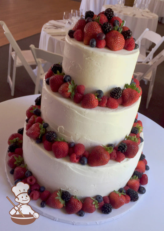 3-tier cake with white icing and decorated with a light texture and fresh strawberries, raspberries, blueberries and blackberries.