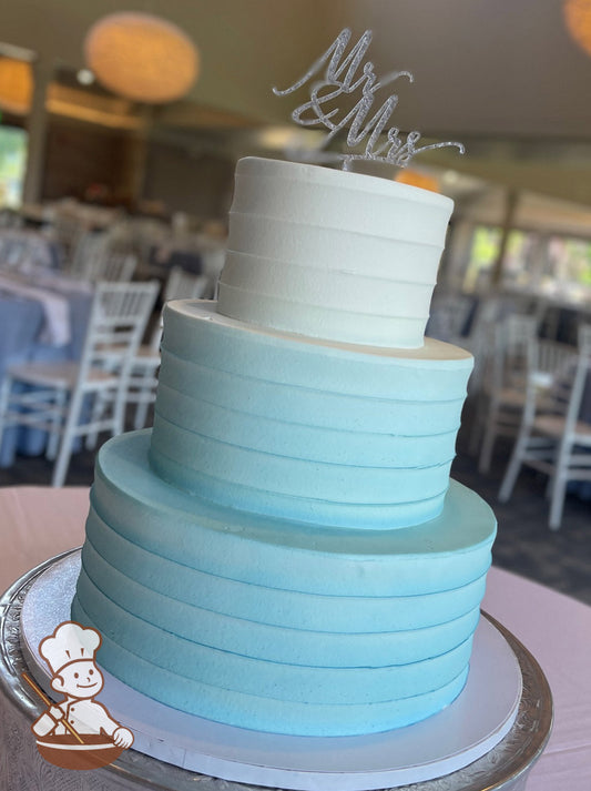 Cake with white icing decorated with a light horizontal texture and an airbrushed ombre coloring starting with a light-blue at bottom to white.
