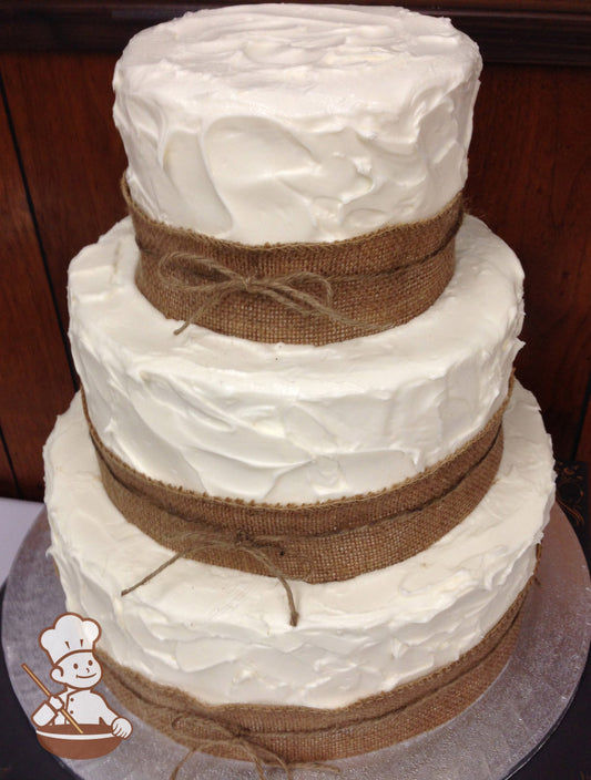 3-tier cake with white icing and decorated with a heavy all over texture and a burlap ribbon on the base of each tier.