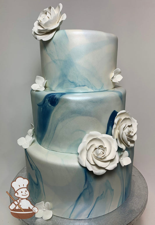 3 tier round cake with blue marble fondant cover and decorated with white sugar roses and hydrangeas.