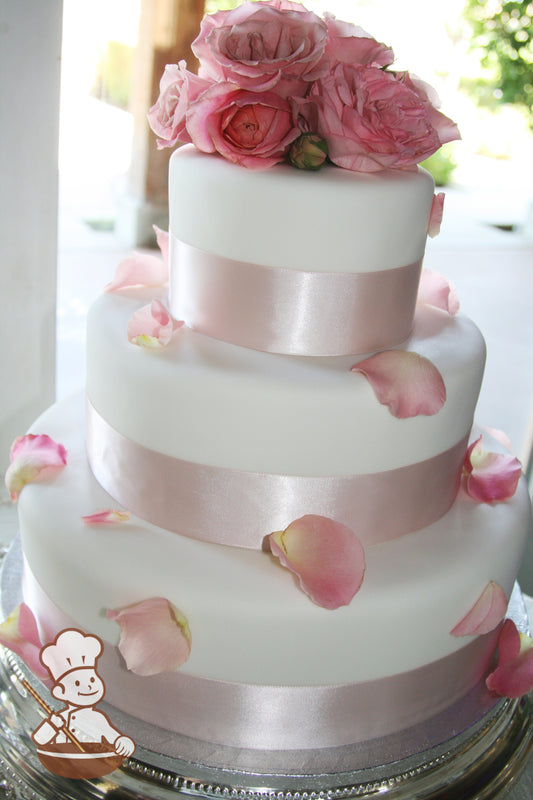 3 tier white fondant wedding cake wrapped with 2 inch pink santin ribbon and decorated with fresh roses and petals.