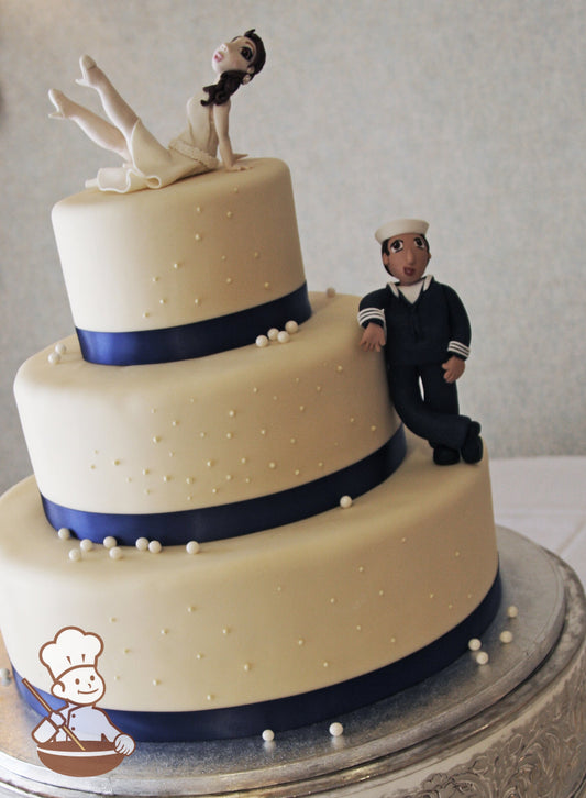 3 tier fondant wedding cake with navy blue satin ribbon wrap and decorated with sugar pearl beads and finished with sailor cake topper.
