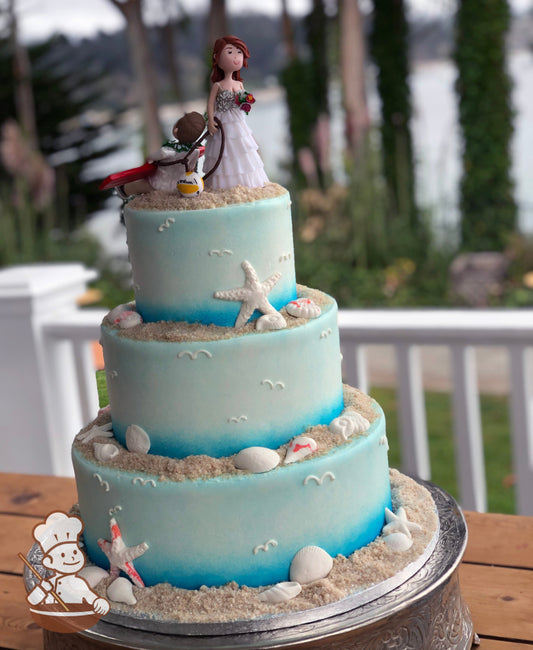 3-tier cake with brown sugar sand and sea shells on top of each tier, along with the cake walls sprayed blue like water and sky, piped seagulls.
