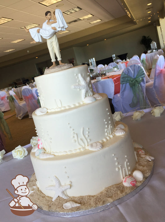 3-tier white cake with kelp bubbles and seashells. Bottom base is decorated with brown sugar sand.