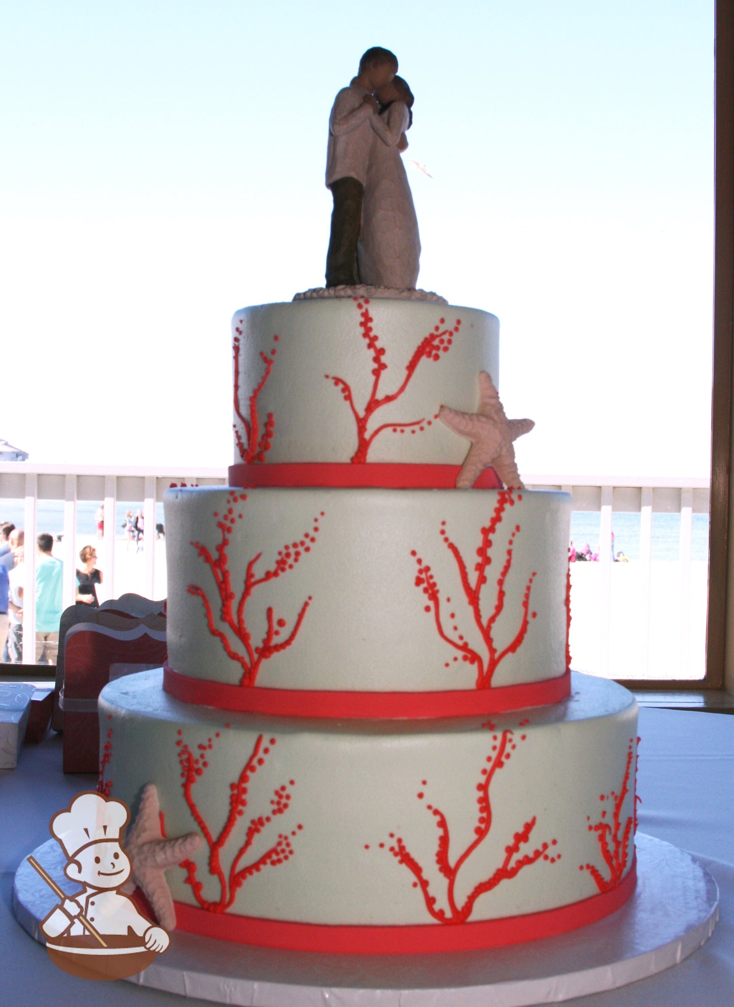White 3-tier cake with piped orange-red corals and orange-red band. Decorated with Starfish.