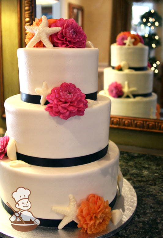 3-tier cake with black ribbon and decorated with sea shells and fresh flowers.