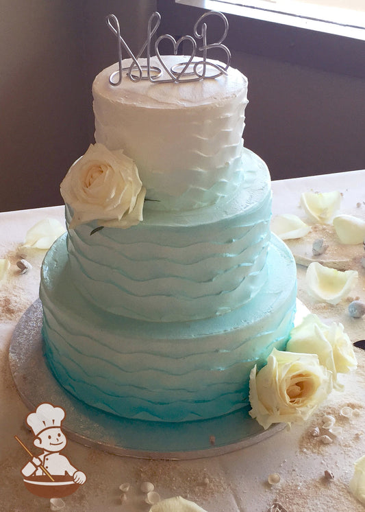 3-tier cake with wavy horizontal textures and sprayed with a gradient blue.