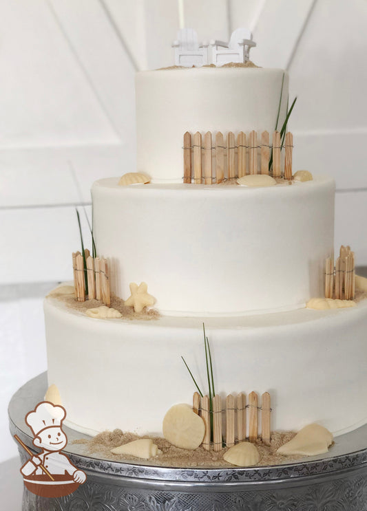 3-tier cake with smooth white icing and decorated with wood picket fences, white chocolate seashells and sugar "sand".