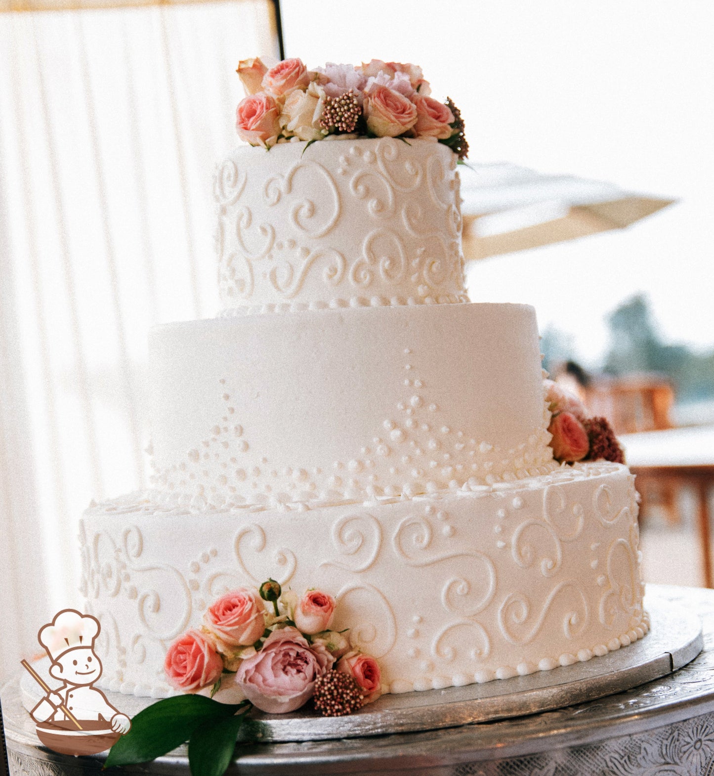 3-tier cake with smooth white icing and white buttercream scrolls on the bottom and top tier and white buttercream dots in the middle tier.