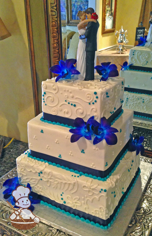 3-tier cake with smooth white icing and white buttercream scrolls and white buttercream tridot piping's with a navy-blue satin ribbon.