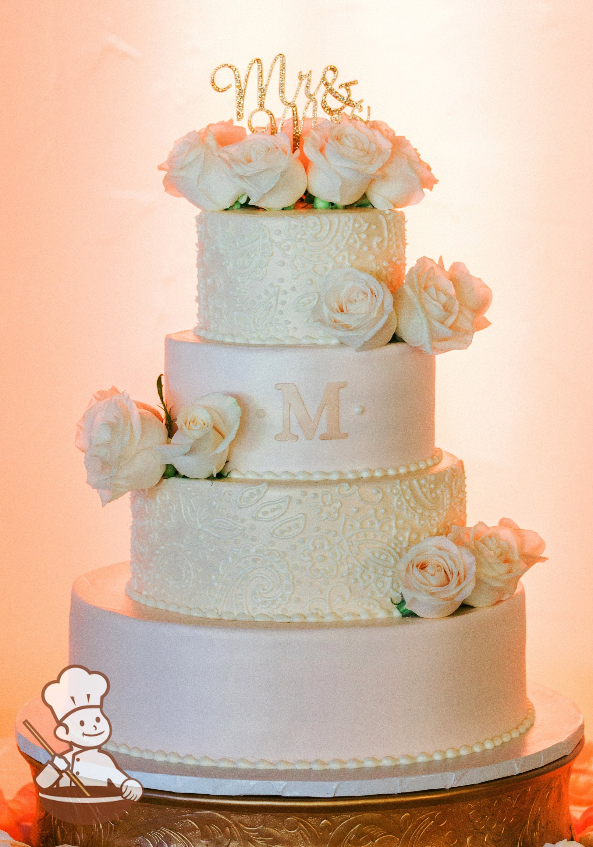 4-tier cake with blush-pink icing on the bottom and third tier and white smooth icing on the second and top tier with piped flowers & scrolls.
