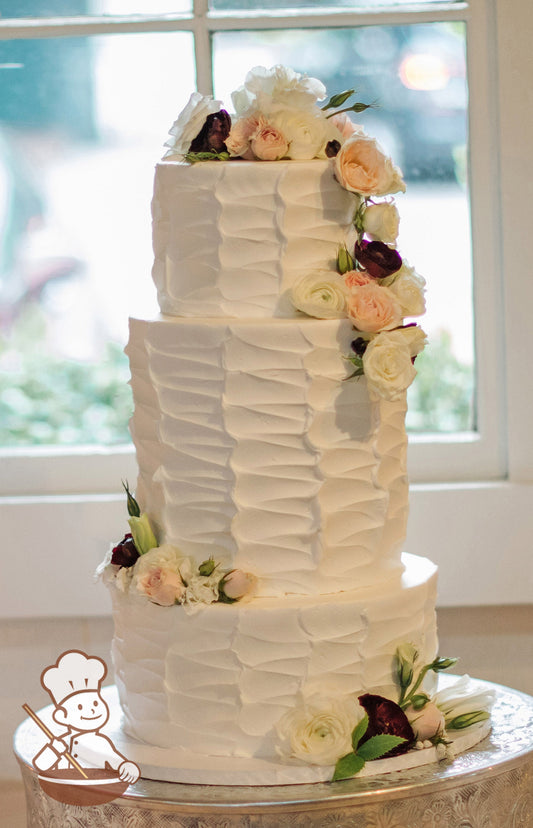 3-tier cake with a white vertical texture and a tall middle tier with fresh flowers in white, blush-pink and burgundy colors.